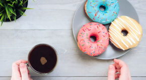 Tre donuts ligger på et fat ved siden av en kopp med kaffe