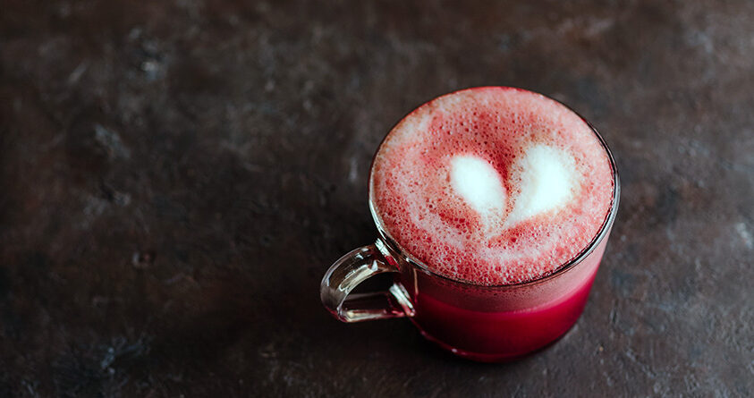 En kopp med red velvet-latte står på et svart underlag