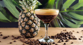 Et glass med espresso martiki står på en benk foran en ananas