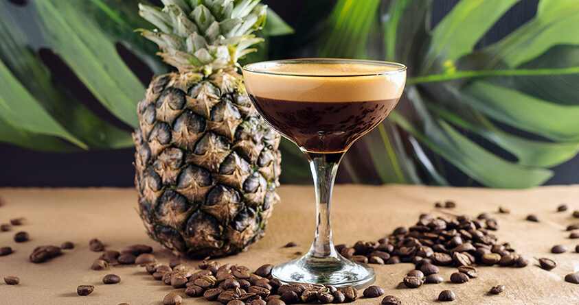 Et glass med espresso martiki står på en benk foran en ananas