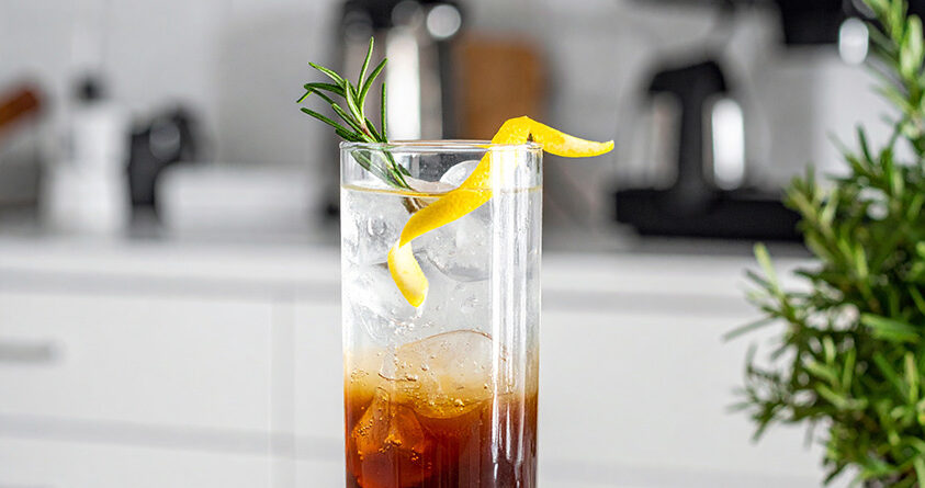 Et glass med kaffe tonic med rosmarin står på en kjøkkenbenk