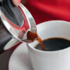 En kvinne heller kaffe fra en perkuator oppi en hvit kopp.