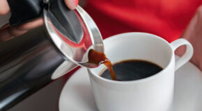 En kvinne heller kaffe fra en perkolator oppi en hvit kopp.