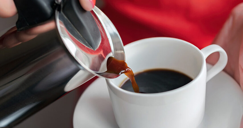 En kvinne heller kaffe fra en perkolator oppi en hvit kopp.