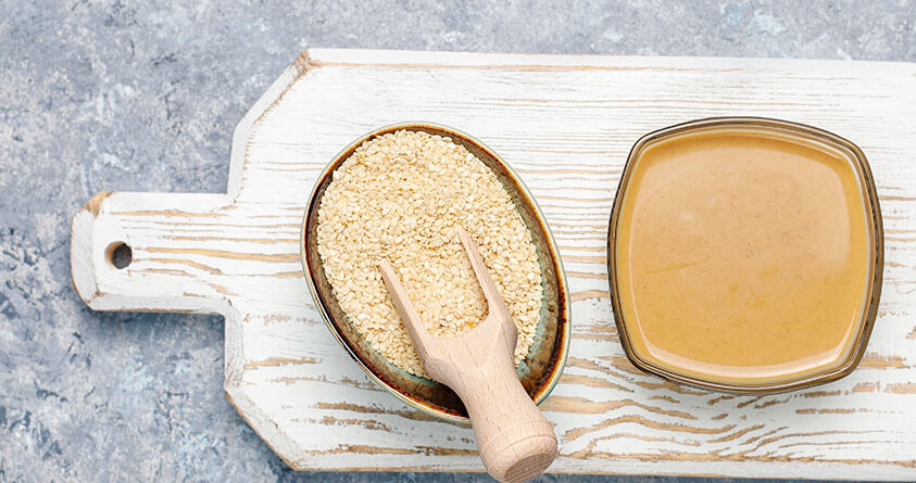 En skål med tahini står ved siden av en skål med sesamfrø