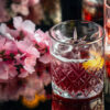 Et glass med kaldbrygget hibiskuskaffe står på et bord ved siden av en blomsterbukett