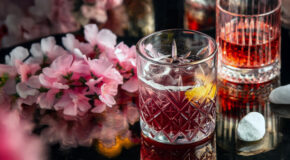 Et glass med kaldbrygget hibiskuskaffe står på et bord ved siden av en blomsterbukett
