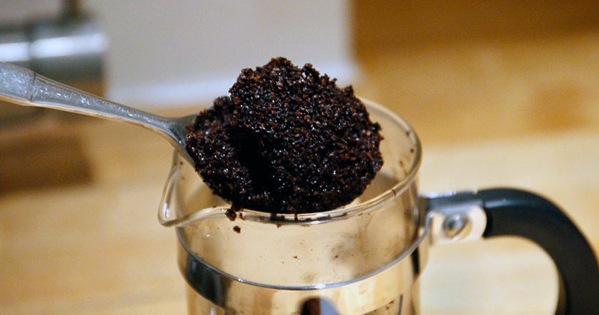 En skje med kaffegrut tas opp fra en presskanne.