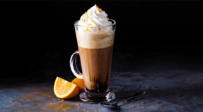 Et glass med mocca står på en mørk benk ved siden av en oppkuttet appelsin