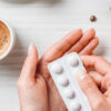En kvinne holder et pillebrett ved siden av en kopp med kaffe