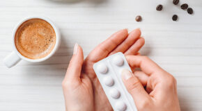 En kvinne holder et pillebrett ved siden av en kopp med kaffe