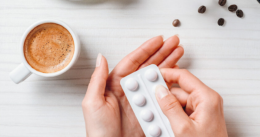 En kvinne holder et pillebrett ved siden av en kopp med kaffe