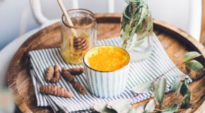 En kopp med gurkemeielatte står på et serveringsbrett