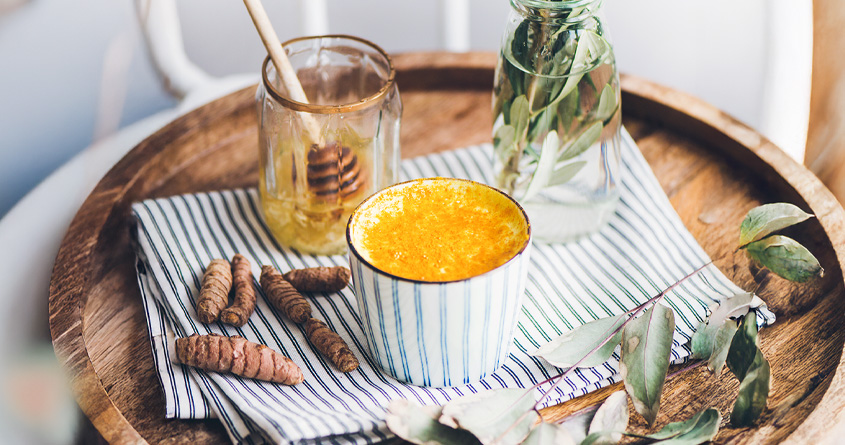 En kopp med gurkemeielatte står på et serveringsbrett