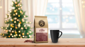 En pose med Sidamo Etiopia-kaffe fra Coffee of the World står på et lyst trebord sammen med en svart kaffekopp. I bakgrunnen står et pyntet juletre.