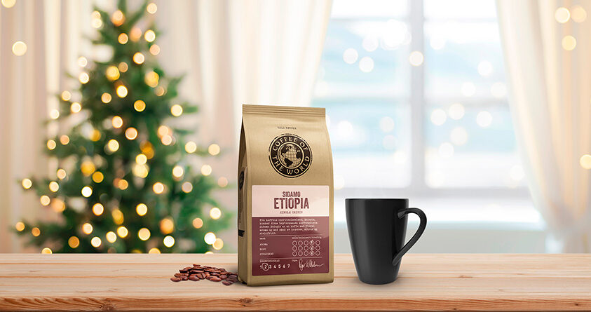 En pose med Sidamo Etiopia-kaffe fra Coffee of the World står på et lyst trebord sammen med en svart kaffekopp. I bakgrunnen står et pyntet juletre.