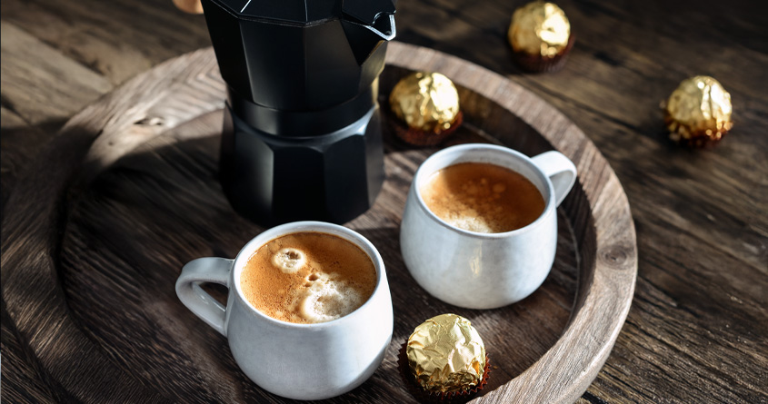 To små kopper med colada-kaffe og en mokkakanne står på et serveringsbrett i tre