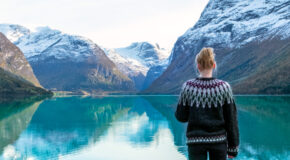 En kvinne med ullgenser står foran et vann, omringet av norske fjell