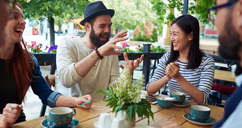 En vennegjeng sitter på kafé og snakker sammen og ler