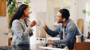 En mann og en kvinne skåler med to kaffekopper over kjøkkenbenken