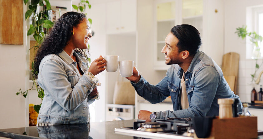 En mann og en kvinne skåler med to kaffekopper over kjøkkenbenken