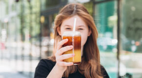 En kvinne holder en kopp med sprudlende espresso med appelsin opp mot kameraet