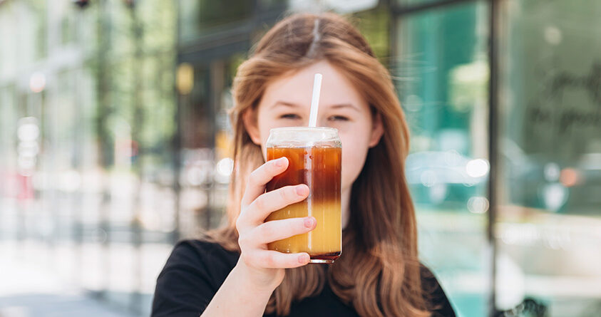 En kvinne holder en kopp med sprudlende espresso med appelsin opp mot kameraet