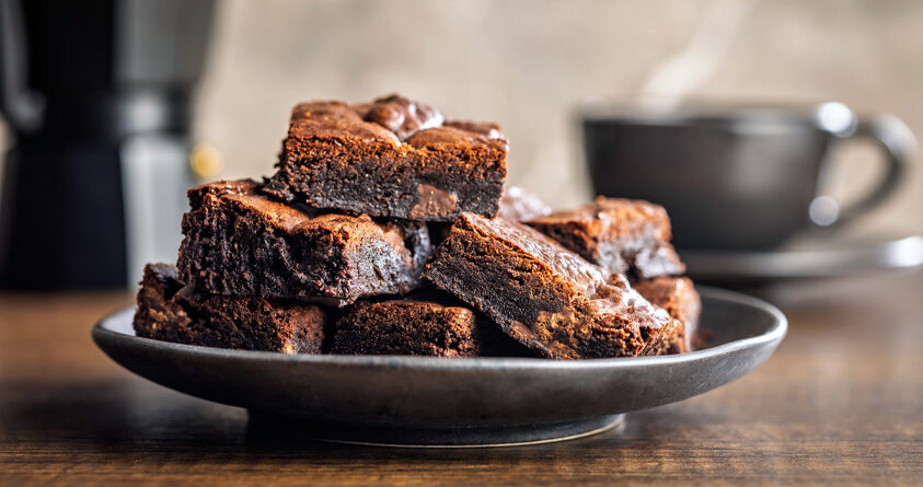 Et fat med brownies står foran en mokkakanne og en kaffekopp