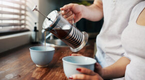 En mann heller kaffe fra en presskanne oppi to kopper