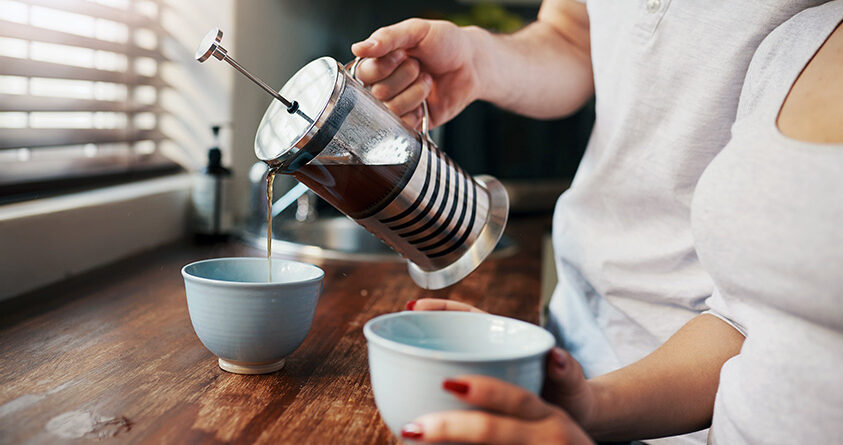 En mann heller kaffe fra en presskanne oppi to kopper