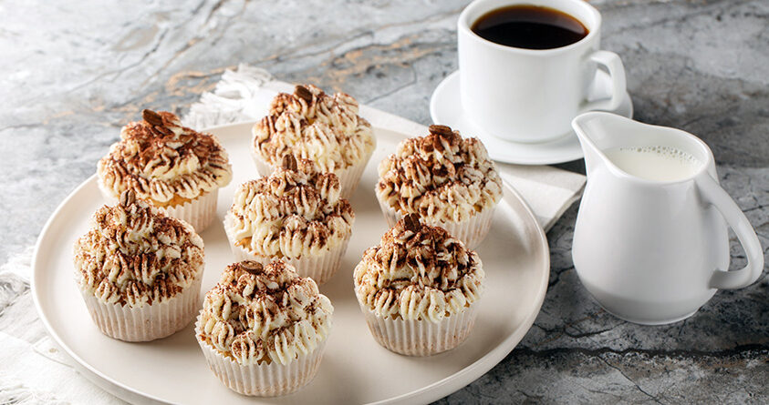 Tiramisu-muffins står på en hvit asjett ved siden av kaffekopp og en mugge med melk