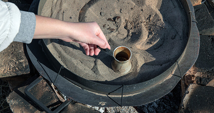 En liten kobberkanne – en såkalt cezve – senkes ned i varm sand for å brygge kaffe