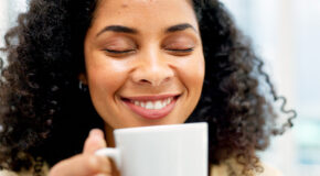 En smilende kvinne med lukkede øyne lukter på en kopp nytraktet kaffe