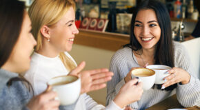 Tre venninner sitter på kafé og drikker kaffe