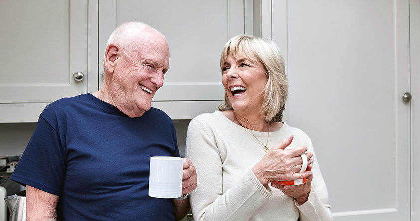 En eldre mann og kvinne drikker kaffe og ler sammen