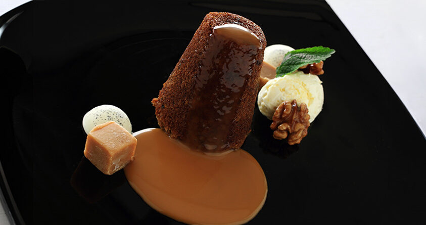 En sticky toffee pudding er pent dandert på en svart tallerken